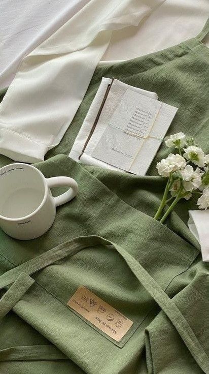 Sage green apron laid out with a mug and notebook